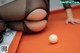 A woman in black stockings and stockings playing pool with a white ball.