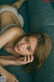 A woman laying on a blue couch with her hand on her chin.