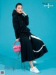 A woman in a black hoodie and pleated skirt posing for a magazine.