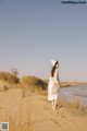 A woman in a white dress and hat standing on a sand dune.