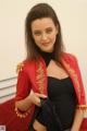 A woman in a red jacket and black top posing on a bed.