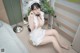 A woman in a white dress sitting on a bed.