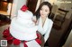 A woman standing next to a white wedding cake with a red rose on top.