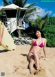 A woman in a pink bikini sitting on the beach.